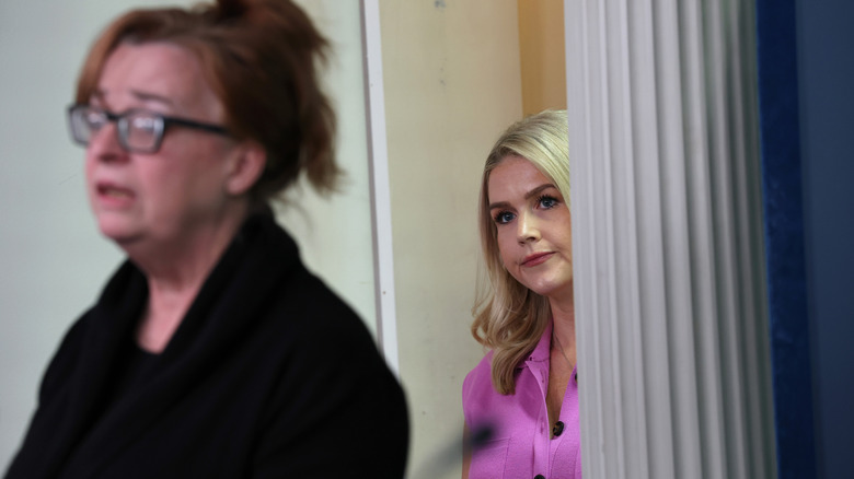 Karoline Leavitt peeking from the doorway as Patty Morin speaks to the press