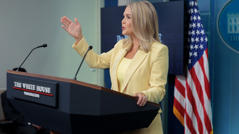 Karoline Leavitt speaking from behind the podium in the press briefing room