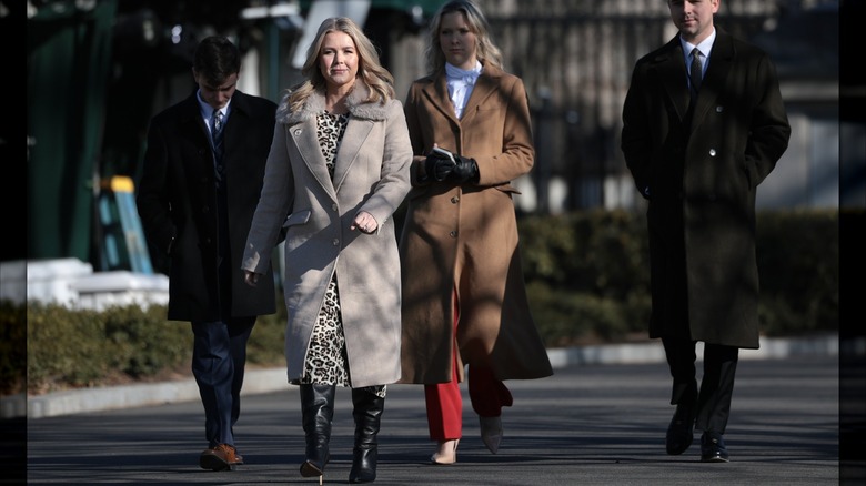 Karoline Leavitt smiling as she walks on black pavement in a winter coat.