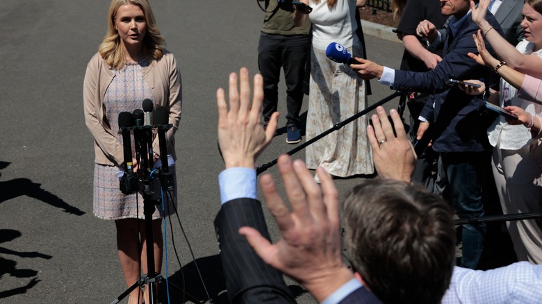 Karoline Leavitt at a microphone, looking out at a sea of press reporters.