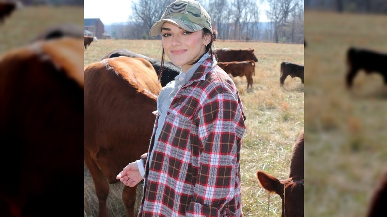 Alexis Wilkins stands in a field with cows.