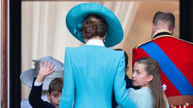 Princess Charlotte peeking over her shoulder as she stands with Kate Middleton's