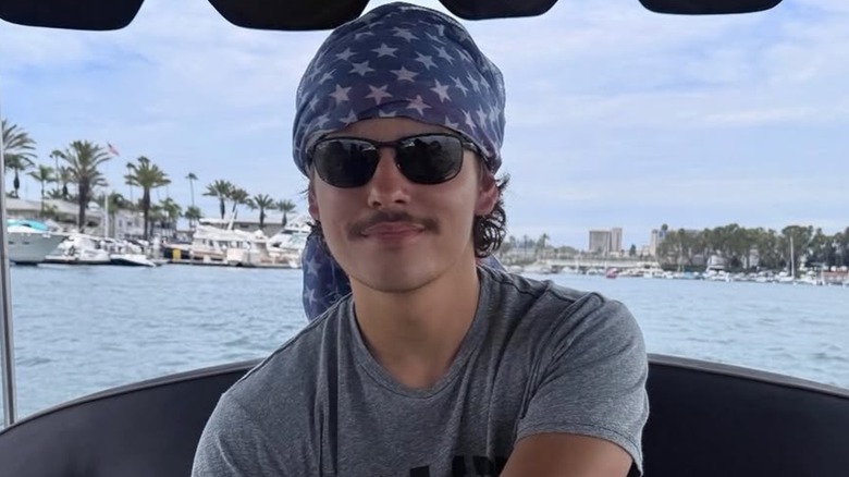 Colin Gosselin driving a boat in a headscarf, sunglasses, and a grey shirt