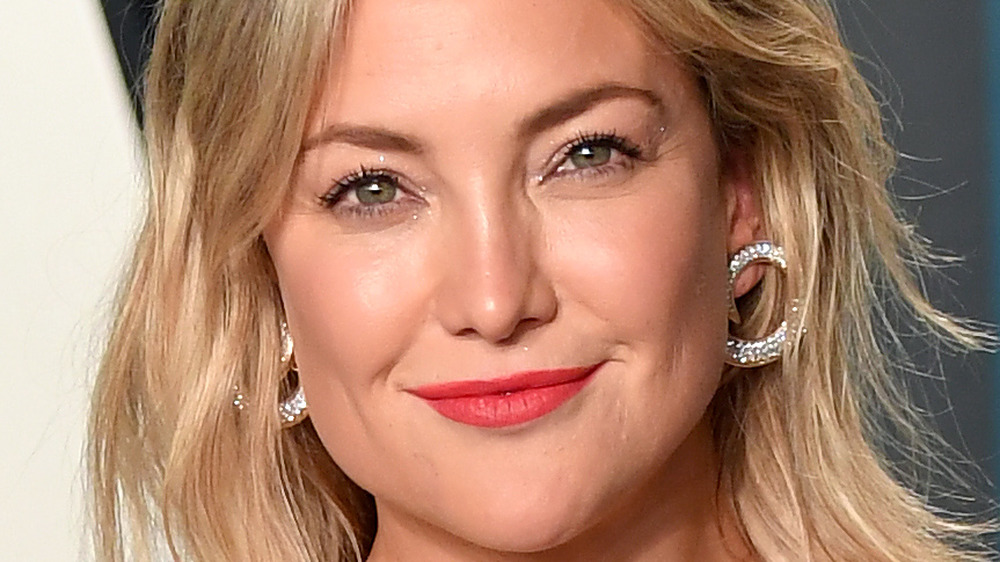 Kate Hudson smiles with red lips and hoop earrings