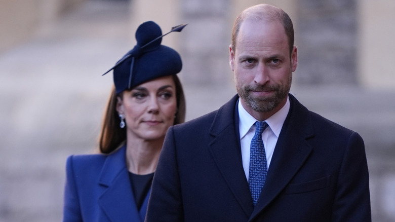 A morbid-looking Prince William walking ahead of a serious-looking Kate Middleton