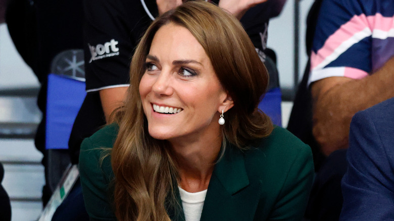 Princess Catherine smiling while watching a match in a green blazer