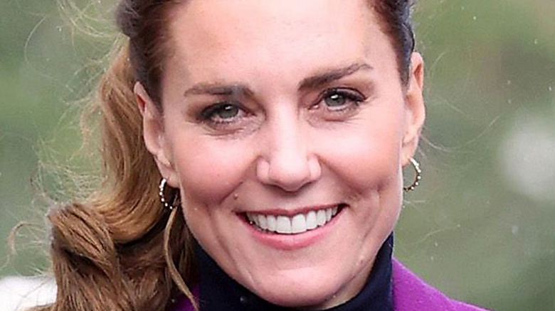 Kate Middleton smiles wearing purple coat.