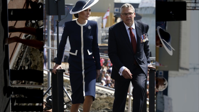 Kate Middleton serious expression as she walks up steps in a navy and white outfit.