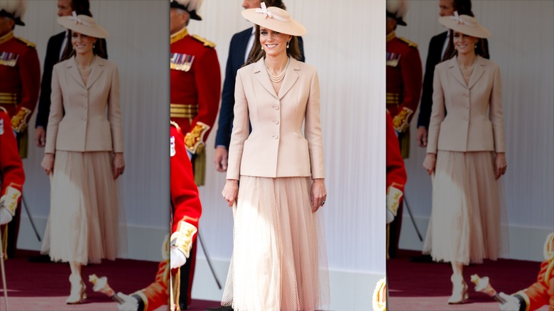Kate Middleton in a peach set with uniformed men behind her.
