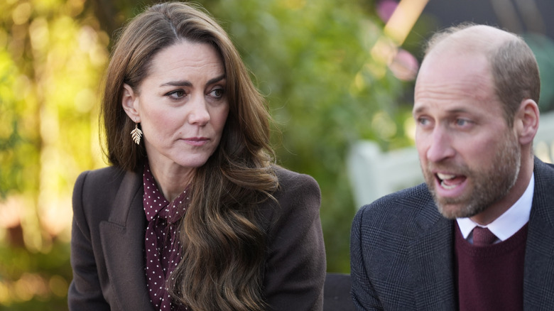 Kate Middleton in burgundy and brown looking at Prince William in burgundy and grey