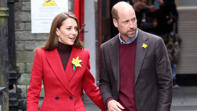Kate Middleton in a red coat with Prince William in a brown coat with a red sweater underneath