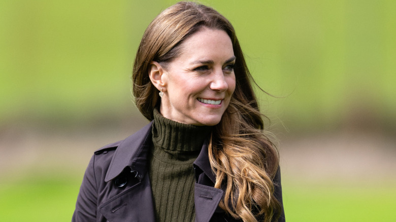 Princess Catherine smiling while looking over her shoulder in a navy coat and green turtleneck