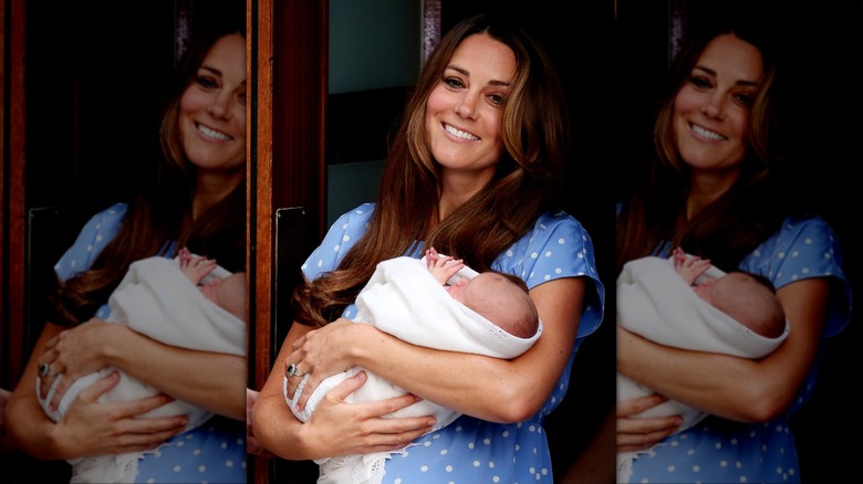Princess Catherine smiling in baby blue dress with white polka dots while holding Prince George