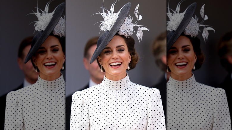 Princess Catherine smiling in a white high neck dress with black dots and a black hat with white feathers