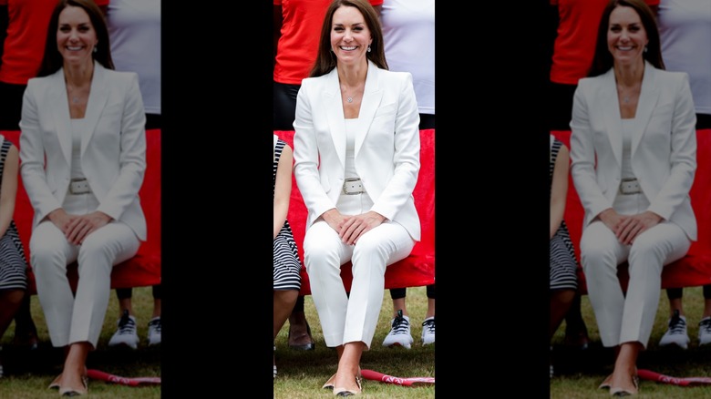 Kate Middleton sits smiling in a white suit at the Commonwealth Games