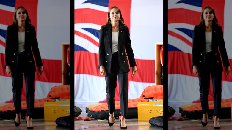 Kate Middleton walking across a stage in a dark suit for a visit to the English navy base