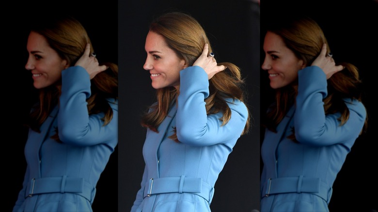 Kate Middleton in an all-blue look, looking out of the corner of her eye while running her fingers through her hair.