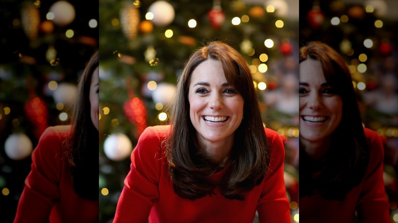 Kate Middleton smiling widely in a red coat in front of a Christmas tree.