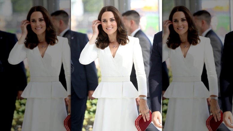 Kate Middleton in an all white dress, tucking her hair behind her ears.