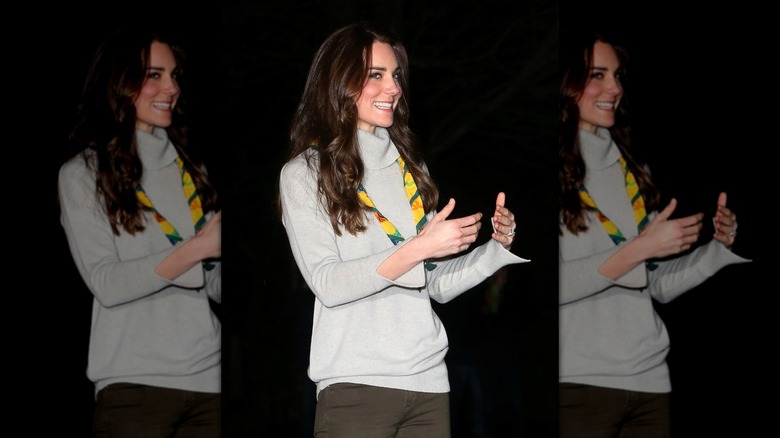 Kate Middleton gesturing with her hands and looking out of the corner of her eyes.