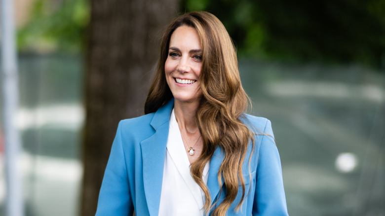 Kate Middleton smiling in a light blue suit with a white shirt underneath it