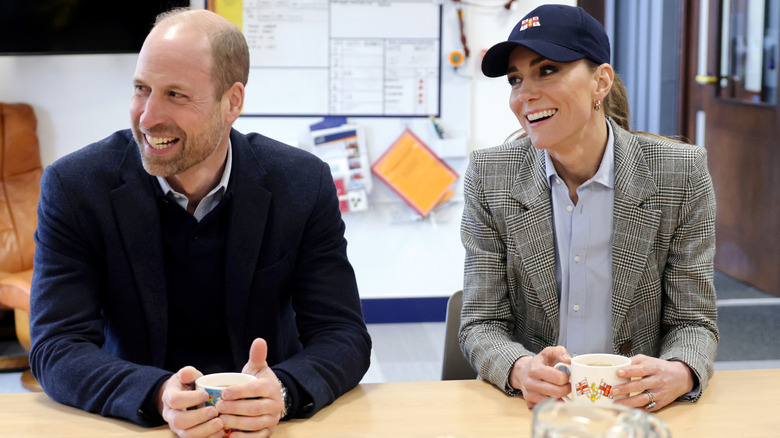 Prince William and Kate Middleton smiling at sitting at a table