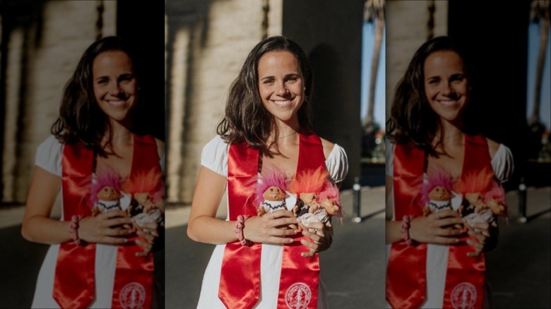 Carrie Monahan smiling in graduation gown holding Troll dolls