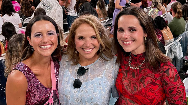 Ellie Monahan, Katie Couric, and Carrie Monahan smile while embracing each other during a concert