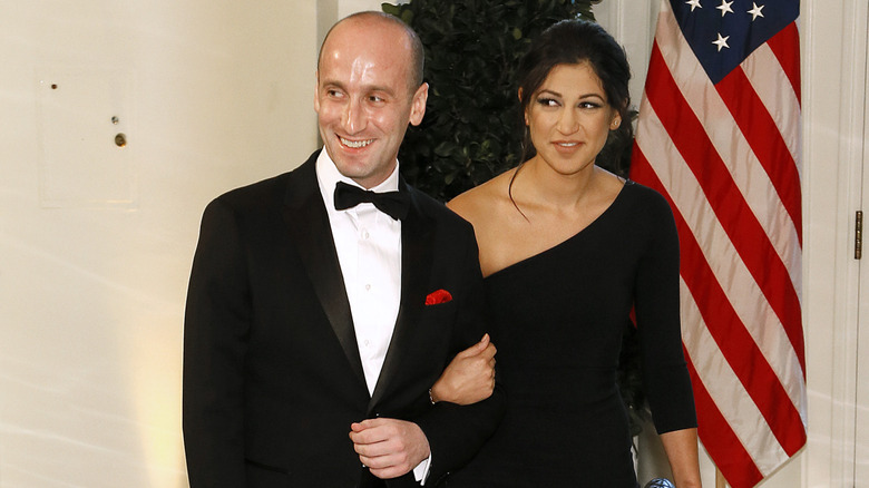 Stephen Miller walking and smiling while arm in arm with his wife Katie
