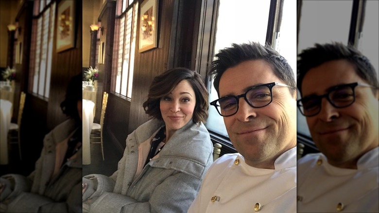 Kavan Smith in a chef's apron sitting with "Love On The Menu" co-star Autumn Reeser