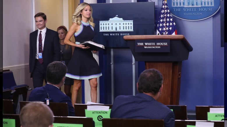 Kayleigh McEnany walking across the stage while wearing a navy dress and holding a binder.
