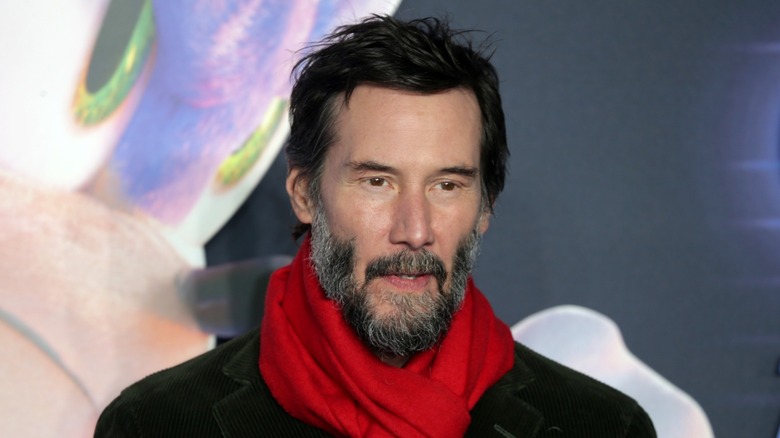 Keanu Reeves smiling in a red scarf