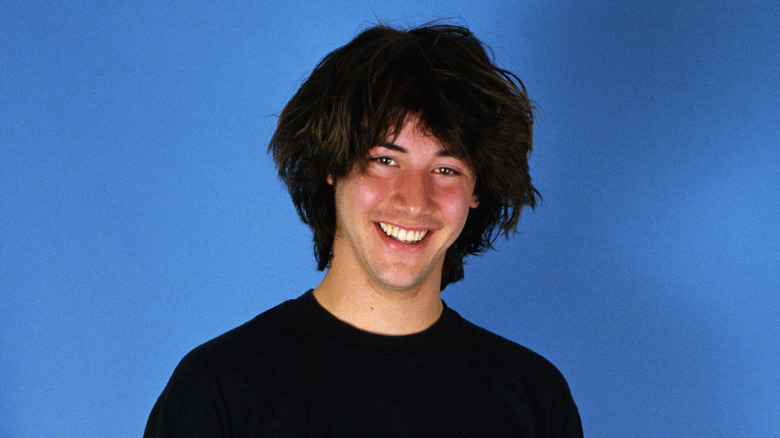 Young Keanu Reeves smiling in front of a blue backdrop