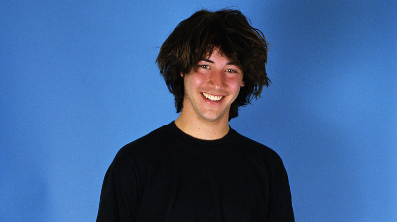 A young Keanu Reeves smiling against blue background