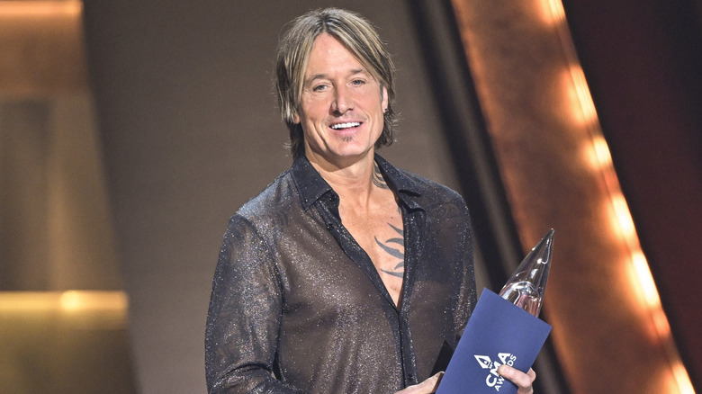 Keith Urban in a black see-through shirt and holding up a trophy