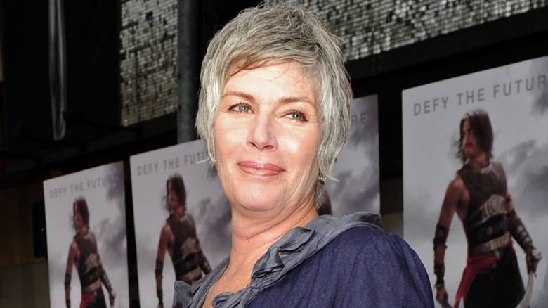 A smiling Kelly McGillis looking over her shoulder while posing on the red carpet in a dark blue top