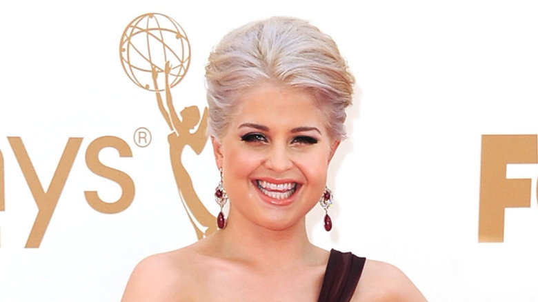 Kelly Osbourne with blonde hair standing in front of a white background