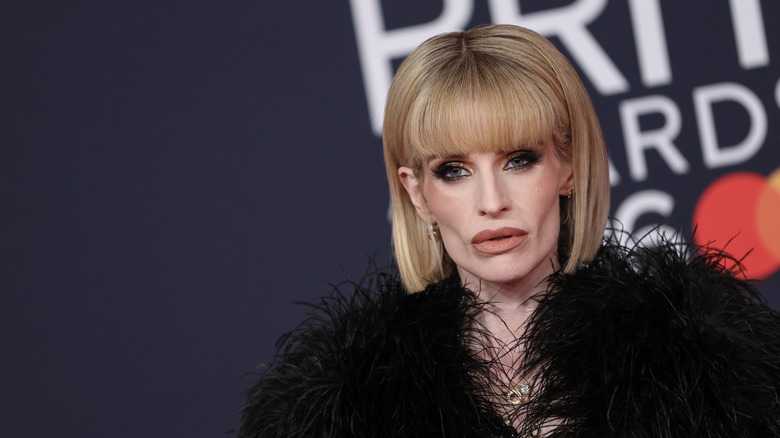 Kelly Osbourne staring while posing at an event in a black feathered outfit