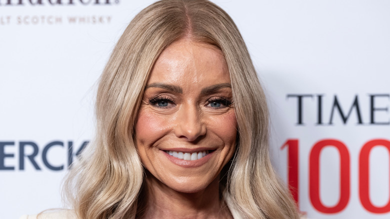 Kelly Ripa smiles and wears her hair down with a soft wave and center part.