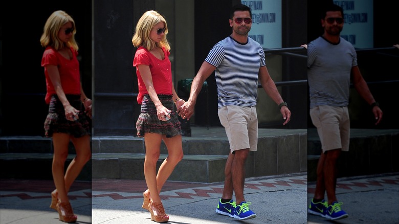 Kelly Ripa wearing a red top and dark gray ruffled miniskirt and holding hands with Mark Consuelos, who is wearing a striped shirt and khaki shorts