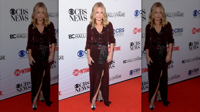 Kelly Ripa posing in a burgundy sequined dress with a black sash belt