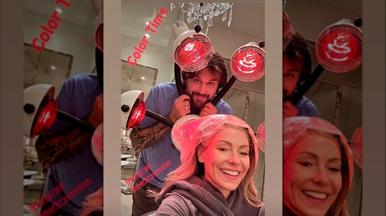Kelly Ripa smiling while sitting in a chair with a plastic bag over her hair.