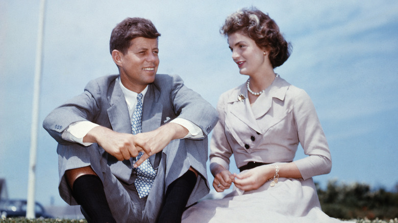 John F. and Jackie Kennedy sitting on lawn against blue sky