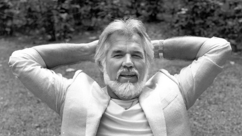 Black and white photo of Kenny Rogers relaxing in a yard in 1985.