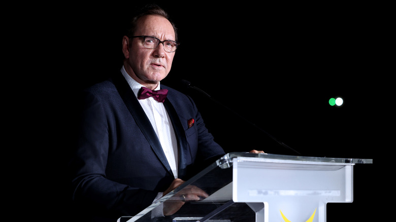 Kevin Spacey giving a speech in a tuxedo and glasses