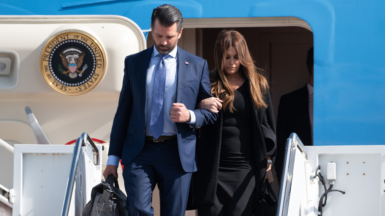 Donald Trump Jr. and Kimberly Guilfoyle exiting Air Force One with their heads down and arms linked.