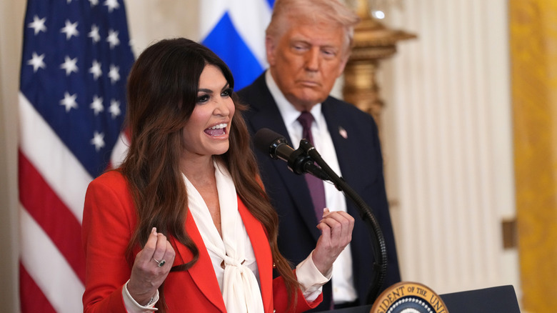 Kimberly Guilfoyle speaking at a podium with Donald Trump standing behind her