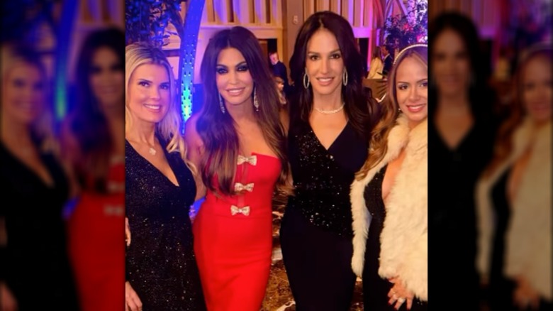 Kimberly Guilfoyle smiling with four women, wearing a red dress with bows down the bodice