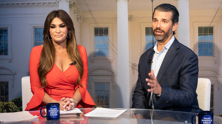 Kimberly Guilfoyle sitting at a desk with Don Jr. talking next to her