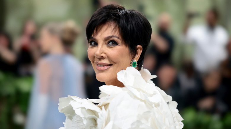 Kris Jenner smiling while looking over her shoulder in a white dress